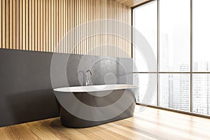 Grey bathtub on wooden floor in bathroom near window, wooden design