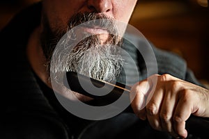 Grey bearded man with a straightener, beard styling and care at home