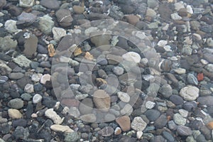 Grey black white brown pebbles stones under water blur