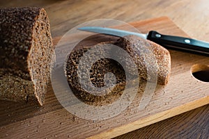 Grey bread with knife on wooden board. Wheat bread slices on cutting board. Bakery products. Crusty grain bread on table