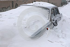 Grey car with a broken rearview mirror under a layer of snow