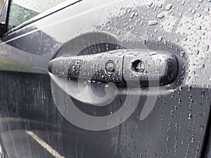 A grey car door handle, covered in rain drops after a storm in the pacific northwest