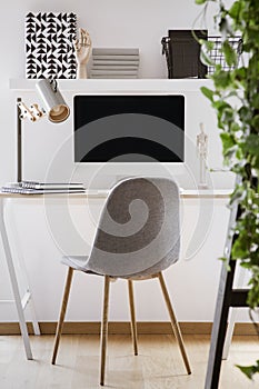 Grey chair at desk with desktop computer and lamp in modern white workspace interior. Real photo