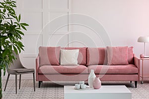 Grey chair next to pastel pink couch with pillows in fashionable living room, copy space on empty wall