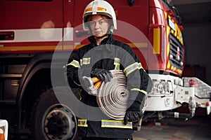 Grey colored fire hose is in the hands. Woman in uniform is at work in department