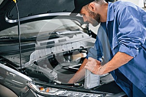 Grey colored oil can in hands. Auto mechanic working in garage. Repair service