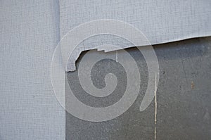 A grey concrete wall of a room with wallpaper half torn off