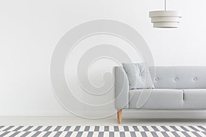 Grey couch in white minimal apartment interior with copy space on empty wall. Real photo