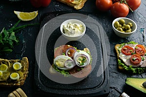 Grey cutting board with sandwich with tomato, egg and purple onion and white souce