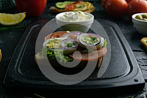 Grey cutting board with sandwich with tomato, egg and purple onion and white souce