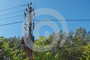 Grey distribution transformer connected to incoming power cables from above and output cables from below in red corrugated tube