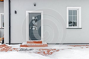 Grey entrance door with glass leading to a private house. Winter, snow