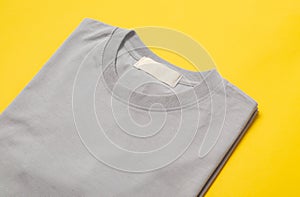 Grey folded t-shirt with blank tag for your design isolated on yellow background.