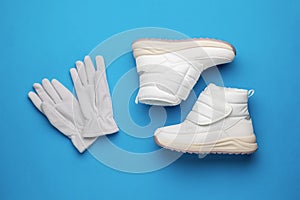 Grey gloves and white winter sneakers on a blue background. Flat lay