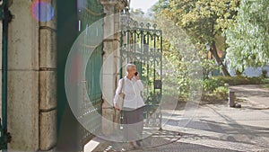 Grey hair woman calling mobile phone waiting friend in park view through gate.