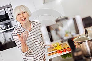 Grey hair woman using modern smartphone, cooking food, recording video photo