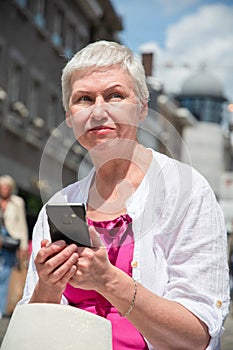 Šedá vlasy starý kavkazský žena v létě oblečení chatování v mobilní v město 