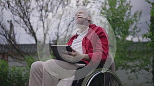 Grey-haired bearded disabled old man smiling holding diary. Portrait of positive senior Caucasian handicapped retiree