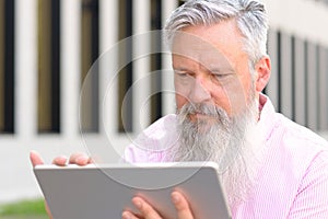 Grey-haired bearded man reading on a tablet