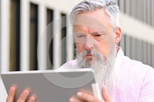 Grey-haired bearded man reading on a tablet