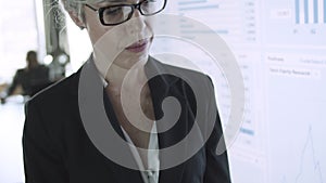 Grey-haired businesswoman in glasses holding tablet and typing