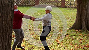 Grey-haired caucasian elderly pensioner couple having fun, spinning around, and dancing in the park, enjoying autumn.