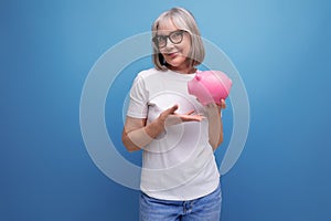grey-haired grandmother keeps her pension in a piggy bank on a studio background with copy space