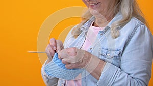 Grey-haired grandmother knitting on yellow background, craft hobby, retirement