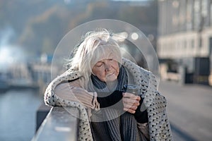 Grey-haired homeless woman standing on the bridge and drinking tea