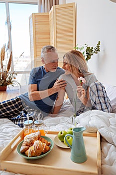 Grey-haired husband looking at his beaming wife while having breakfast