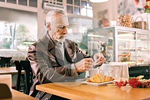 Grey-haired man sitting in French bakery eating croissant and drinking coffee