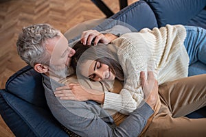 Grey-haired man sitting on the sofa and hugging his wife with tendernes photo