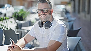 Grey-haired man using smartphone wearing headphones at coffee shop terrace