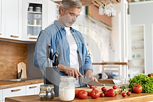 Grey-haired Mature handsome man preparing delicious and healthy food in the home kitchen.