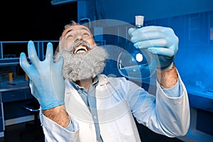 Grey haired scientist celebrating success of scientific experiment and holding flask with reagent