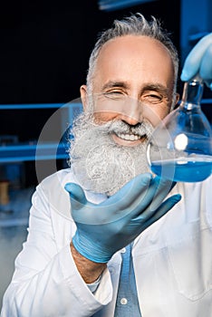 Grey haired scientist in lab coat holding flask with reagent at laboratory