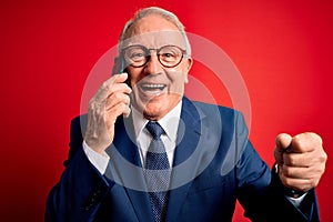 Grey haired senior business man having a conversation talking on smartphone over red background screaming proud and celebrating