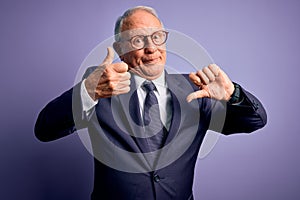 Grey haired senior business man wearing glasses and elegant suit and tie over purple background Doing thumbs up and down,