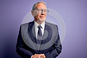 Grey haired senior business man wearing glasses and elegant suit and tie over purple background with hand on stomach because