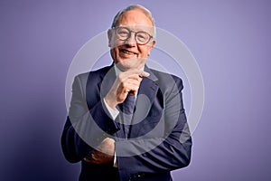 Grey haired senior business man wearing glasses and elegant suit and tie over purple background looking confident at the camera