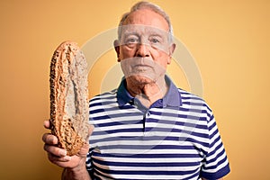 Grey haired senior man holding healthy wholemeal bread over yellow isolated background with a confident expression on smart face