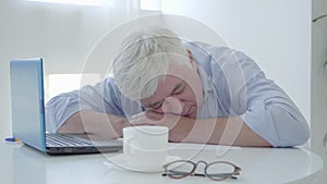 Grey-haired senior man sleeping at the table. Portrait of tired Caucasian businessman exhausted from remote working