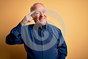 Grey haired senior man wearing casual blue shirt standing over yellow background Smiling pointing to head with one finger, great