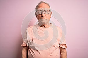 Grey haired senior man wearing glasses standing over pink isolated background with serious expression on face