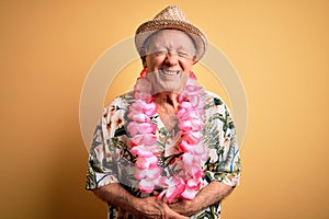 Grey haired senior man wearing summer hat and hawaiian lei over yellow background with hand on stomach because indigestion,