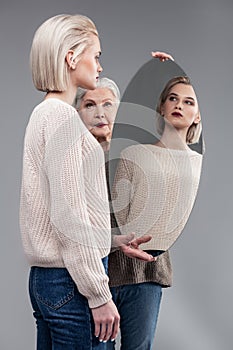 Grey-haired serious mother carrying round mirror while her daughter