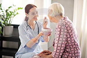 Grey-haired woman eating oatmeal and talking to nurse