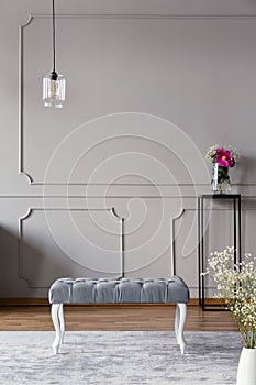 Grey hallway interior with a bench, lamp and flower in a vase on a stand. Real photo. Place for your poster