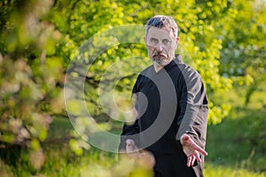 Grey head master in black kimono practices tai chi in a sakura garden