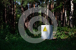 Grey Hinged Power Supply Box in the wood. electrical box with yellow danger warning sign. electricity in remote places